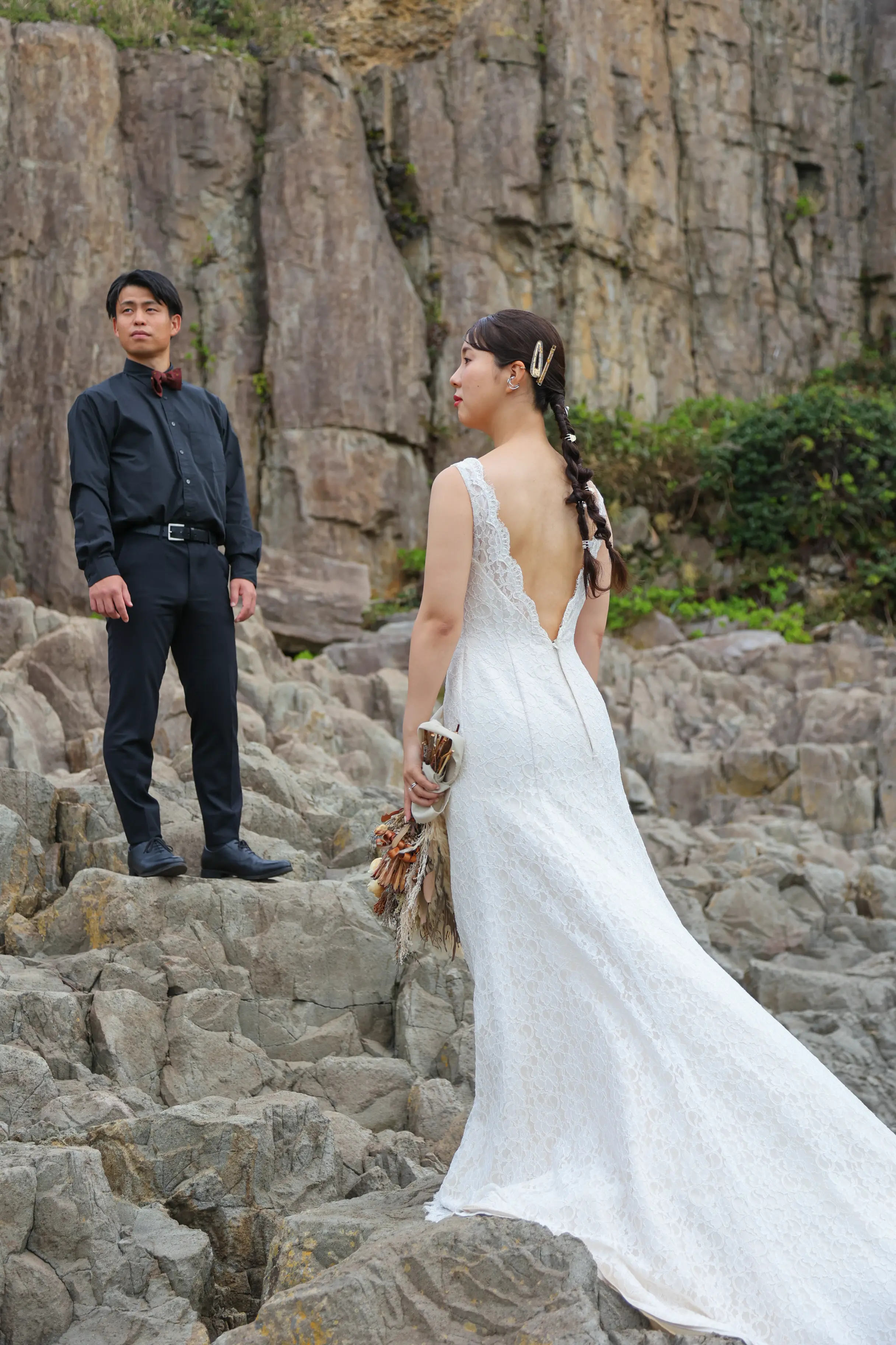 東尋坊の柱状節理を背景に、ブーケを手にした新婦と少し離れて立つ新郎の物語のような構図
