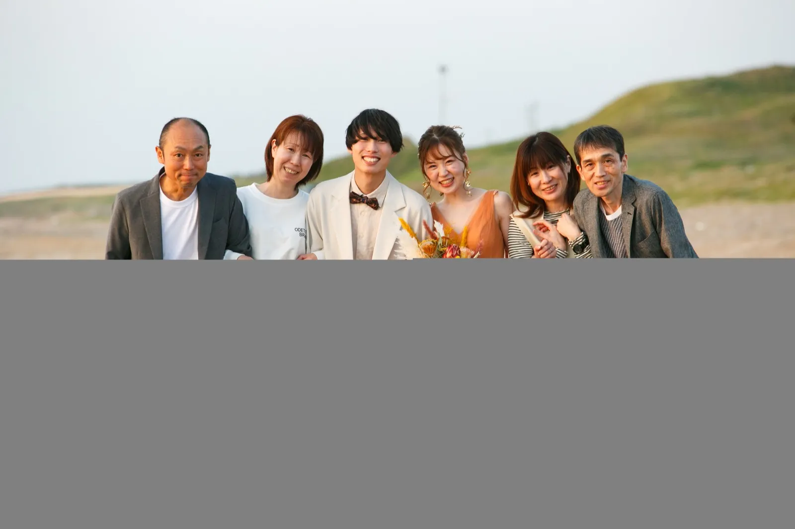 撮影を見守ったご家族と記念撮影する洋装の新郎新婦|金沢・内灘海岸のフォトウェディング