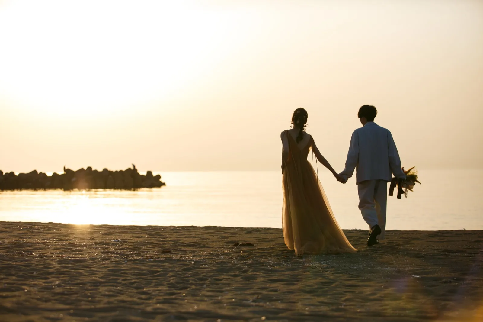 金沢・内灘海岸で夕日を背に寄り添う新郎新婦のシルエット|映画のような一枚