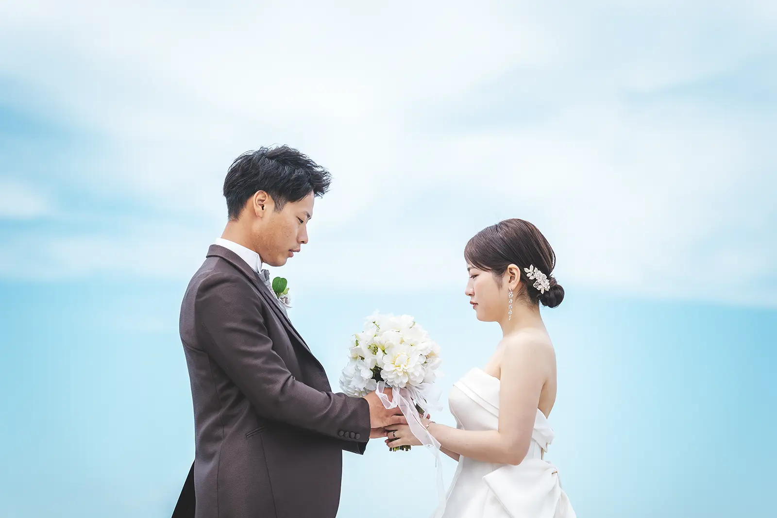 海を背景にブーケを持って向き合う洋装の新郎新婦