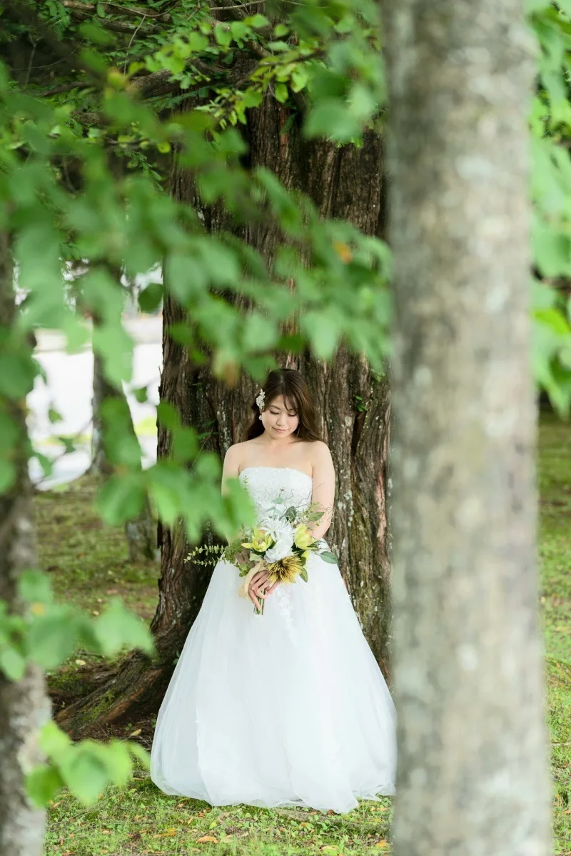 軽井沢の木立で大木を背にブーケを持つウエディングドレスの花嫁|自然豊かなロケーション撮影