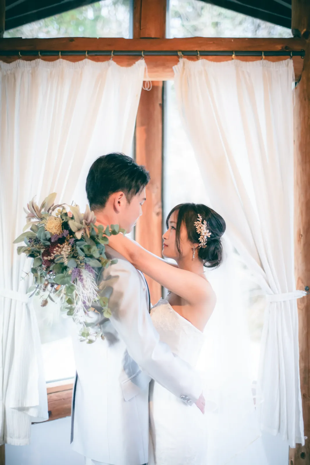 軽井沢・ムーゼの森の窓辺でカーテン越しに向き合う新郎新婦