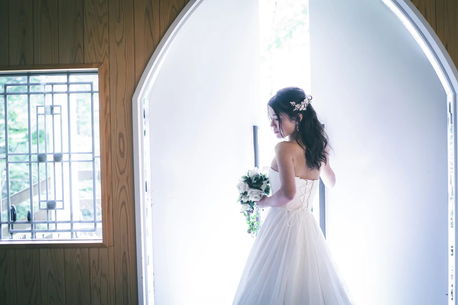 軽井沢の教会で自然光が差し込む扉の前に立つ新婦のウェディングドレス姿