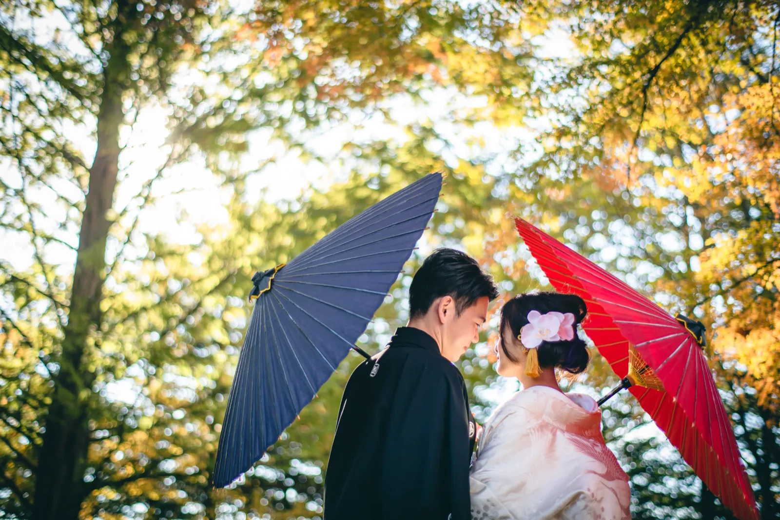 矢ヶ崎公園の紅葉を背景に藍と赤の番傘を持つ和装の新郎新婦