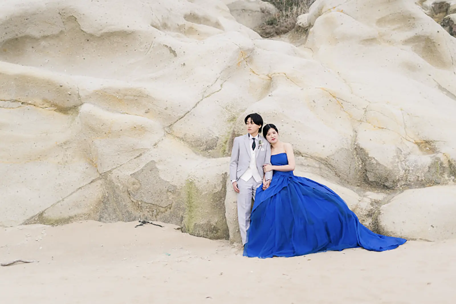 片野海岸の白い岩肌を背景に青いドレスで撮影する新郎新婦