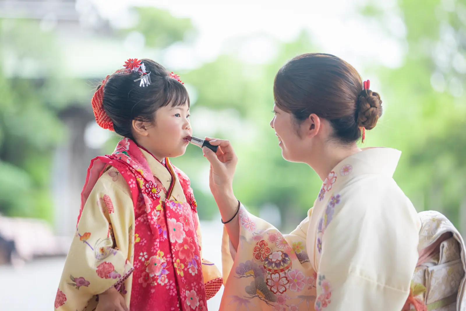 撮影前に3歳の女の子の唇にリップを塗ってあげる訪問着の母、川崎大師での七五三前撮り