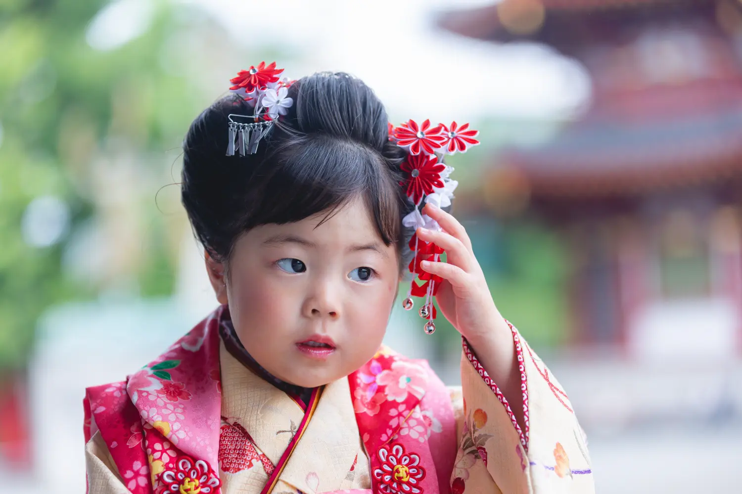 赤い髪飾りに手をふれる3歳の女の子、桜柄の被布と日本髪風の結い上げの七五三前撮り（川崎大師）