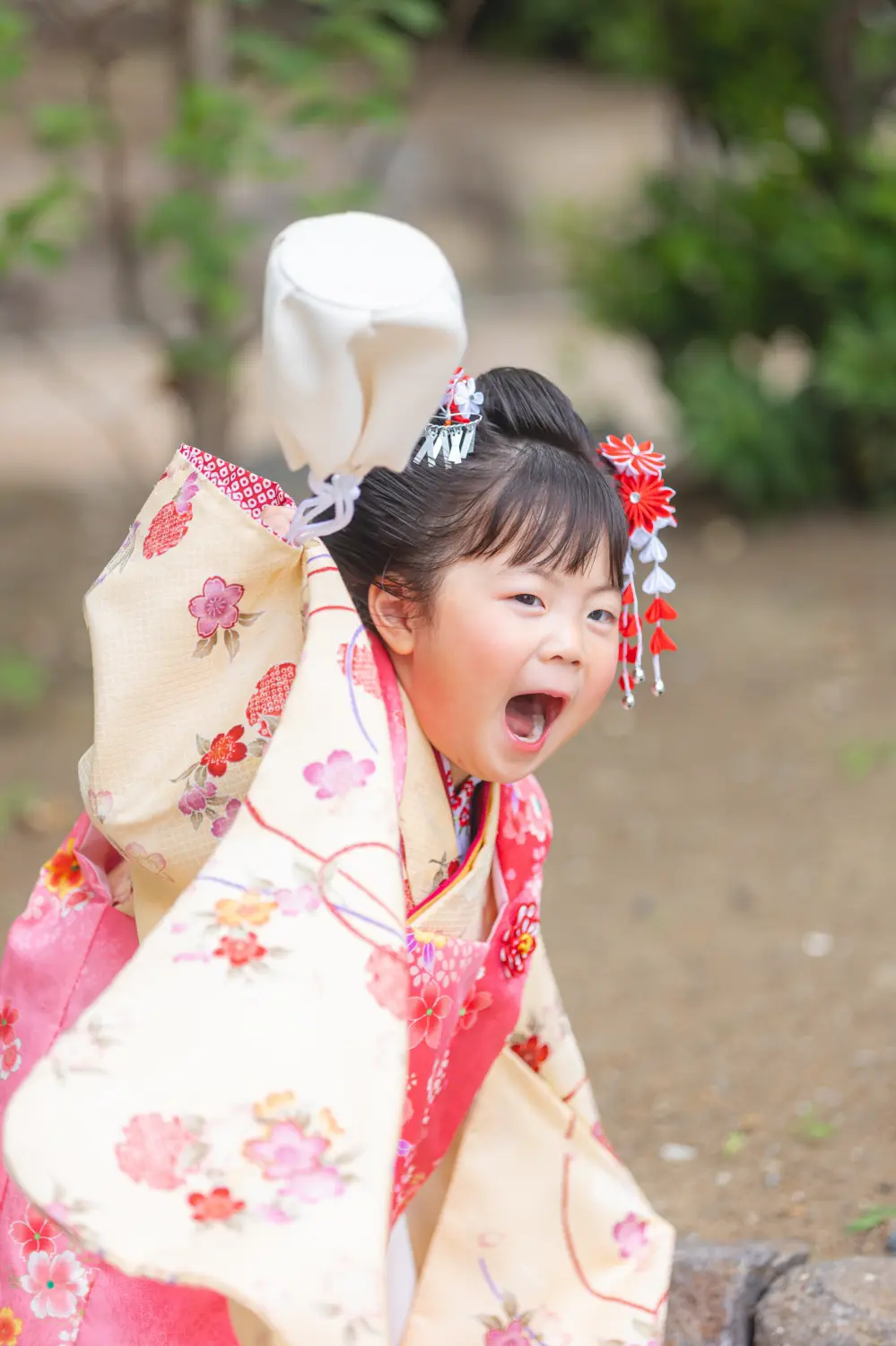 着物の袖を大きく広げて口を開けて笑う3歳の女の子、桜柄の被布姿の七五三前撮り（川崎大師）