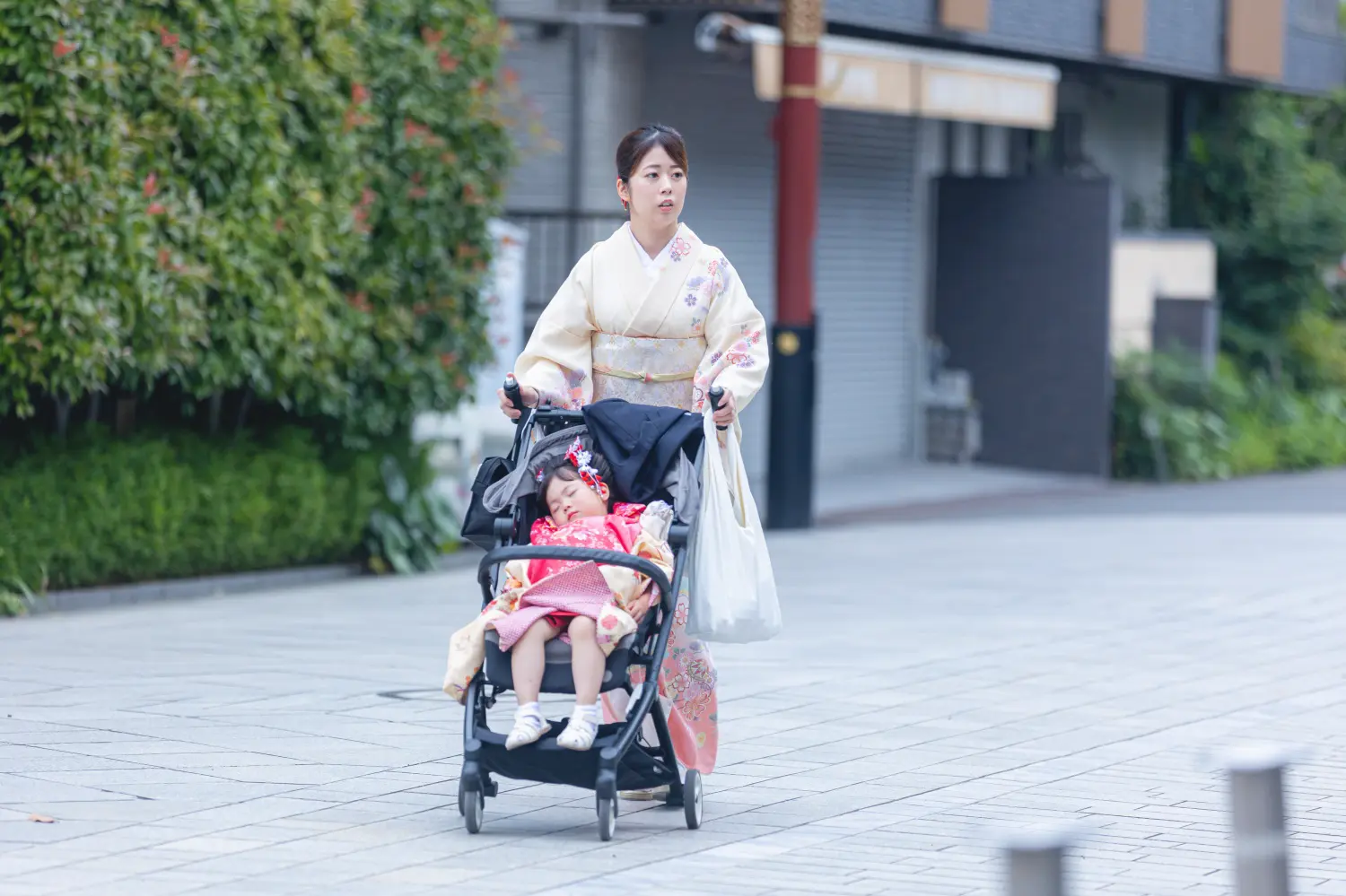 被布姿のままベビーカーで眠る3歳の女の子と、訪問着でベビーカーを押す母、川崎大師での七五三撮影の到着シーン