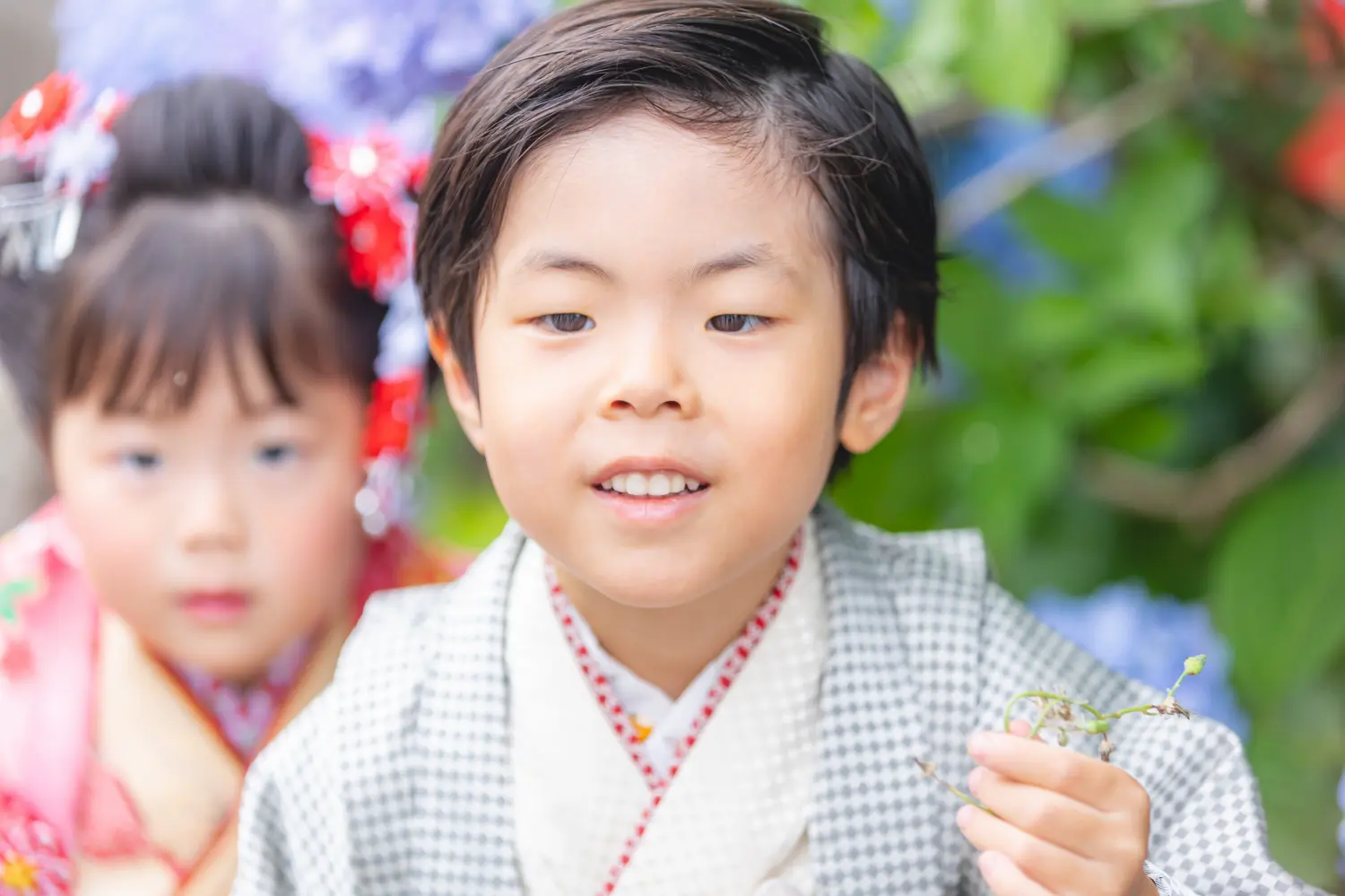 小さな草花を手に笑う5歳の男の子と、後ろでこちらを見る3歳の妹、川崎大師での七五三前撮り