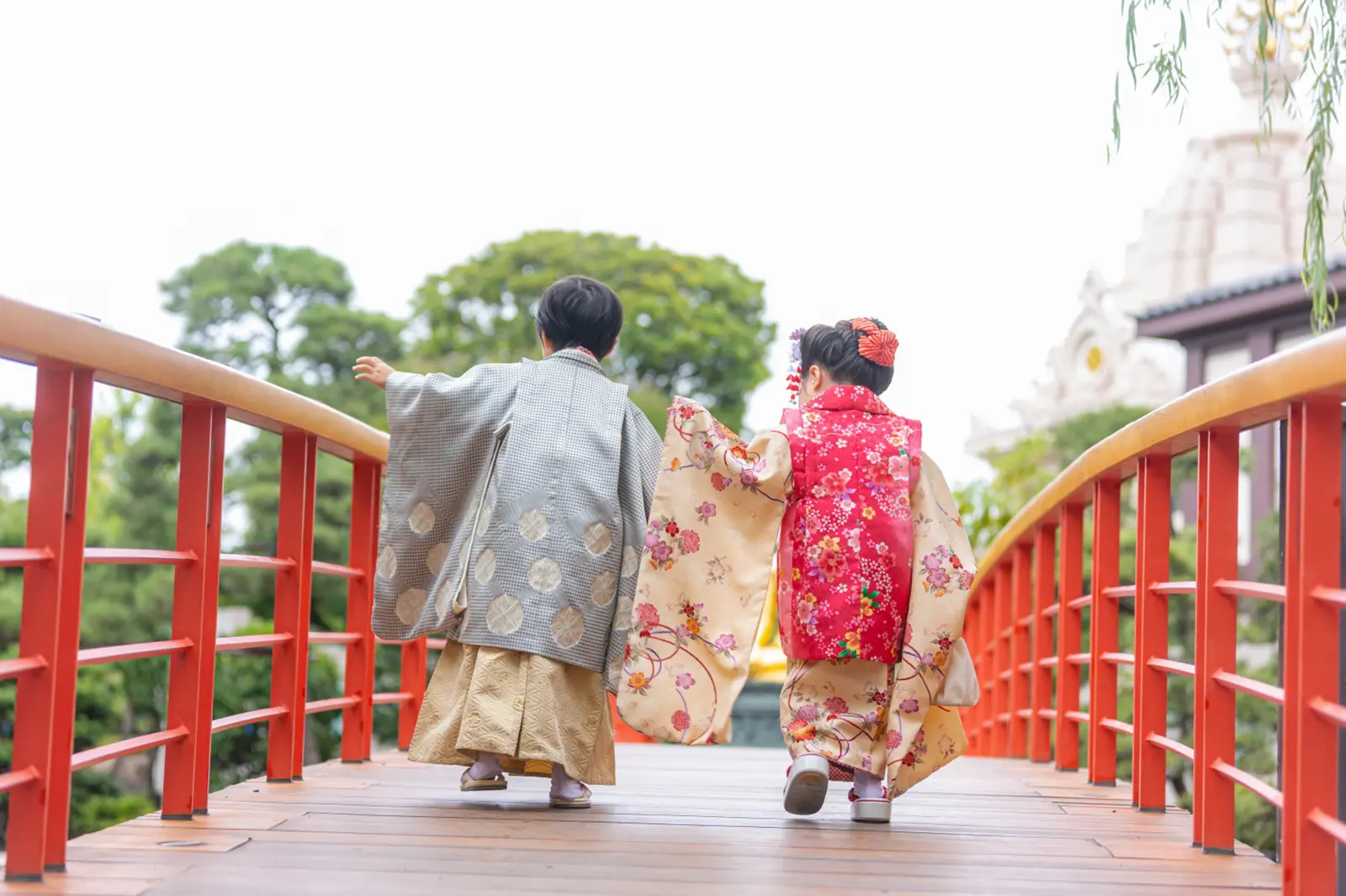川崎大師の朱塗りの太鼓橋を並んで渡る5歳の羽織袴の兄と3歳の被布の妹の後ろ姿、七五三前撮り