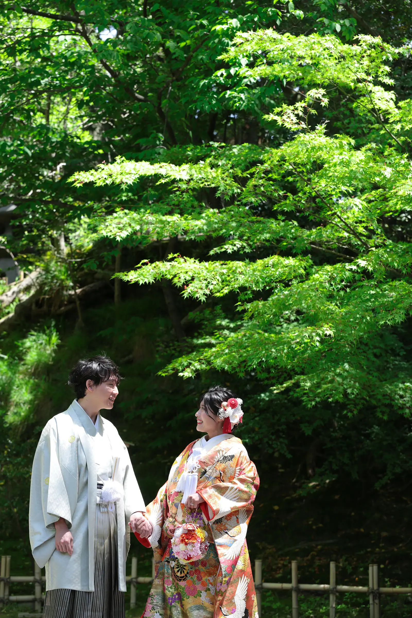 兼六園の新緑を背景に色打掛姿の新婦と紋付袴姿の新郎が見つめ合う和装写真