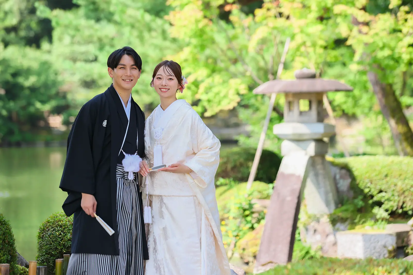 金沢の兼六園でことじ灯籠の近くに立つ白無垢姿の新婦と紋付袴の新郎
