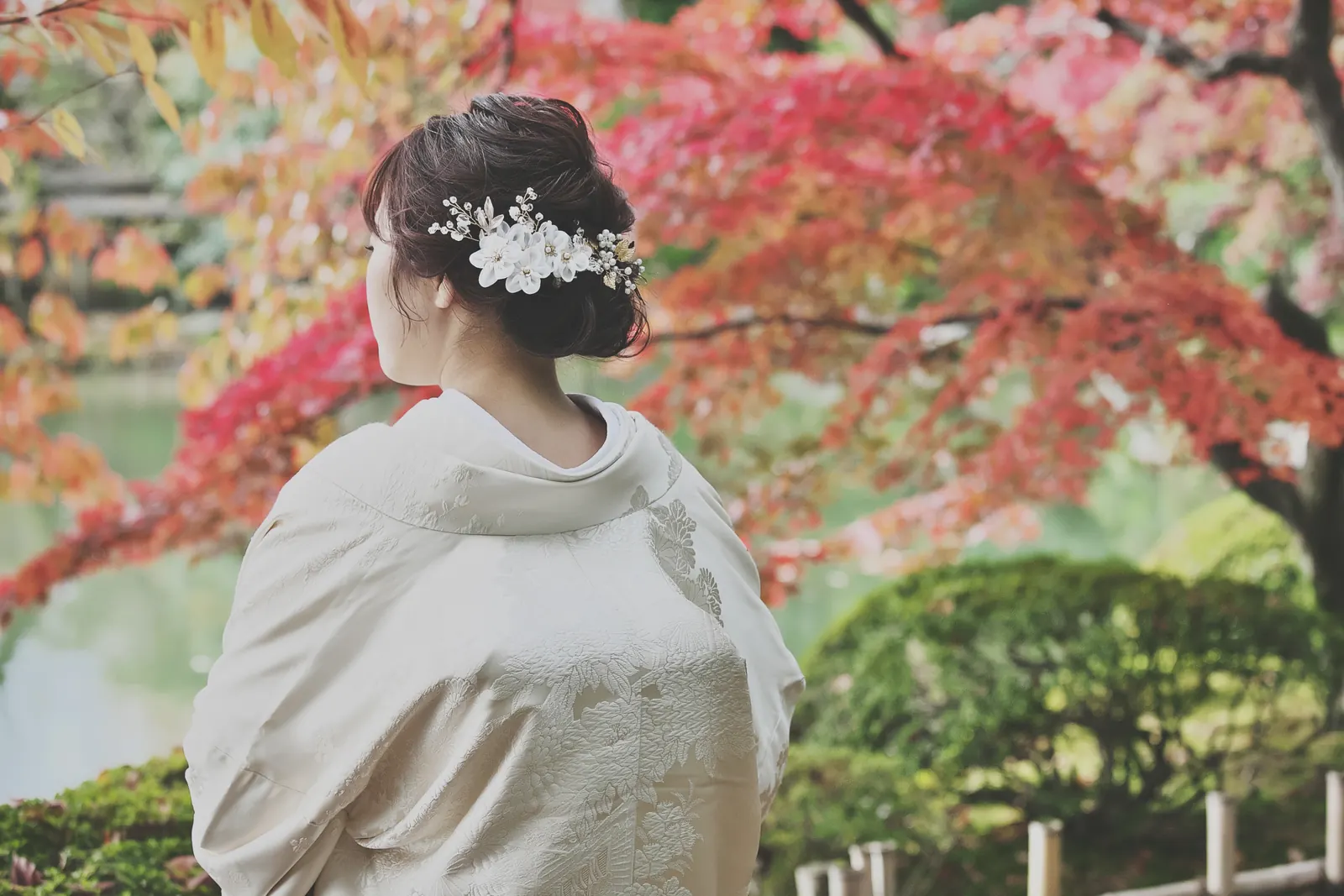 兼六園の色づいたもみじと池を背に立つ、白い髪飾りをつけた白無垢の花嫁の後ろ姿