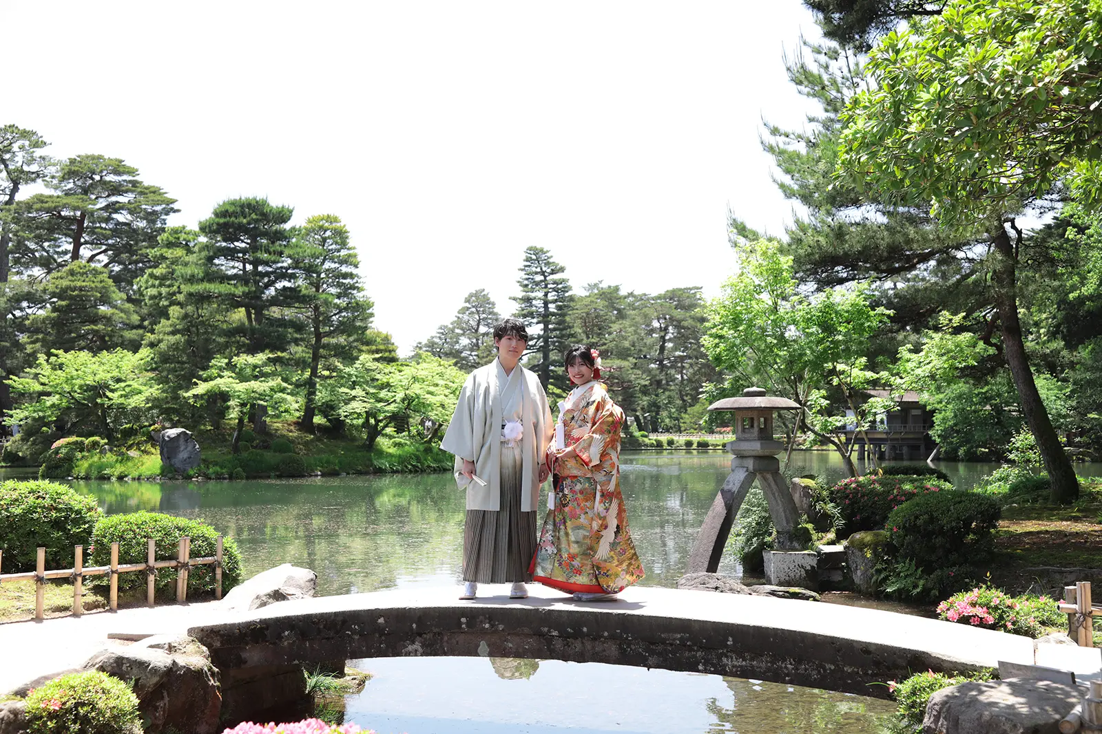 金沢の兼六園で池と石橋を背景に立つ和装姿の新郎新婦
