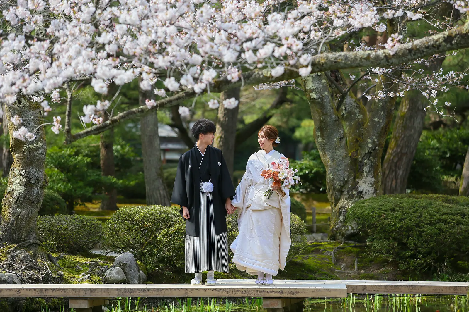 金沢の兼六園で桜が咲く橋の上に立つ和装姿の新郎新婦