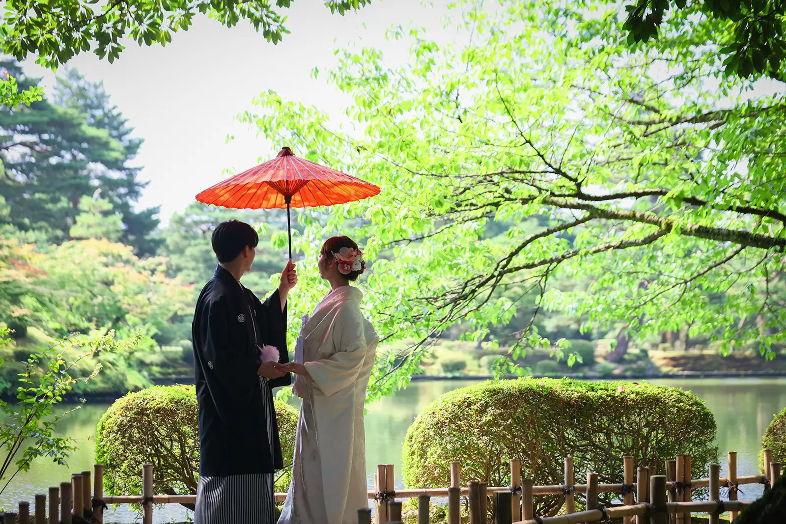 金沢の兼六園で池を背景に和傘を持つ白無垢姿の新婦と紋付袴の新郎