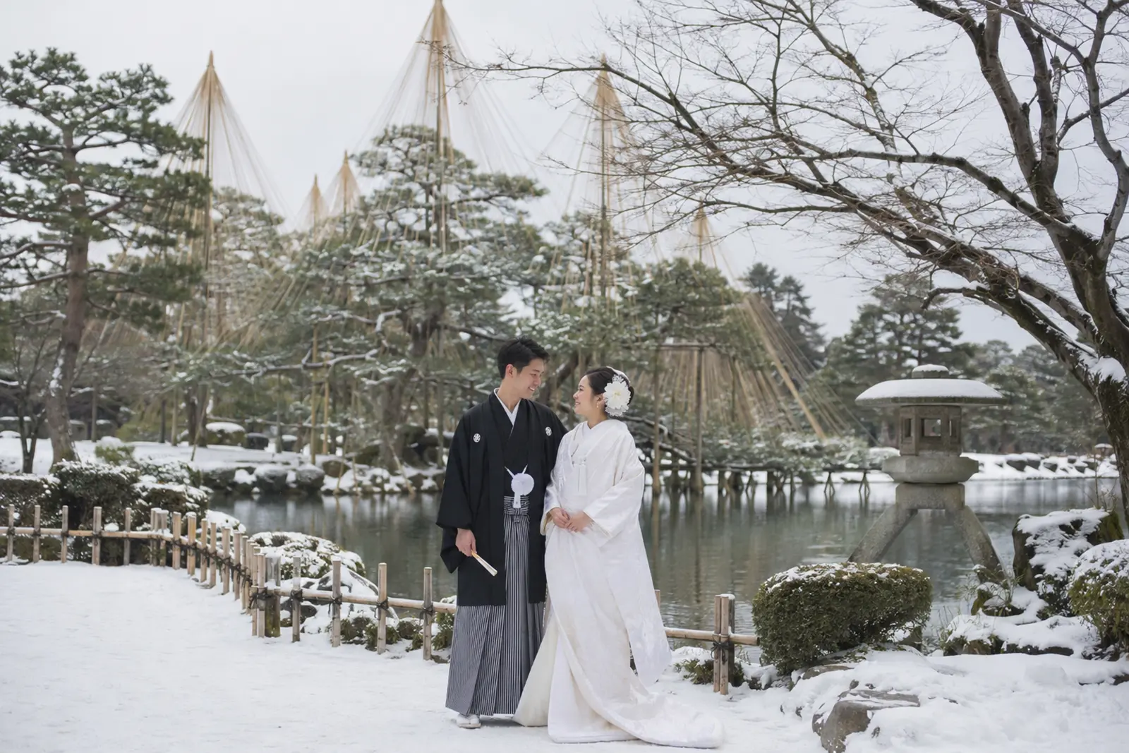 兼六園の雪吊りと雪景色を背景に白無垢姿の新婦と紋付袴姿の新郎が並ぶフォトウェディング写真