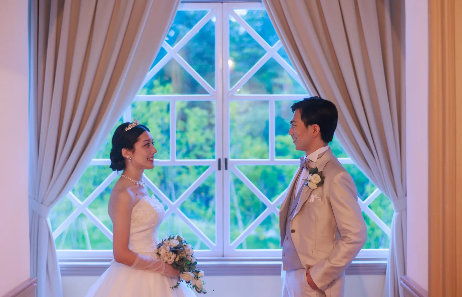 旧三笠ホテルのアーチ窓を背にして向かい合う新郎新婦。窓の外には軽井沢の緑