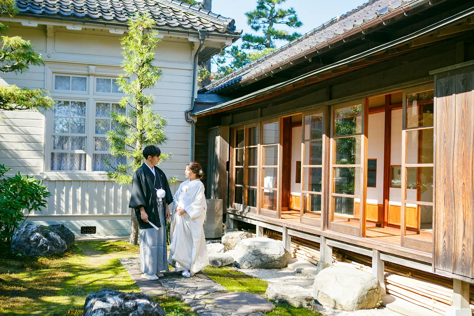 旧高峯家の庭と日本家屋を背景に白無垢姿の新婦と紋付袴姿の新郎が立つ和装前撮り写真
