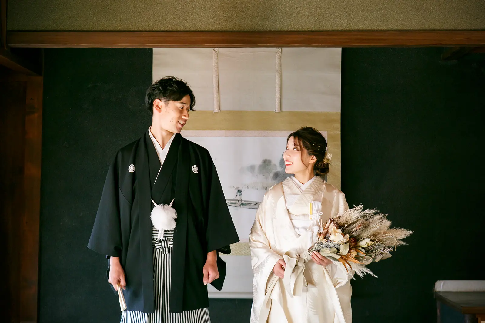旧高峯家の和室で白無垢姿の新婦と紋付袴姿の新郎が笑顔で見つめ合う写真