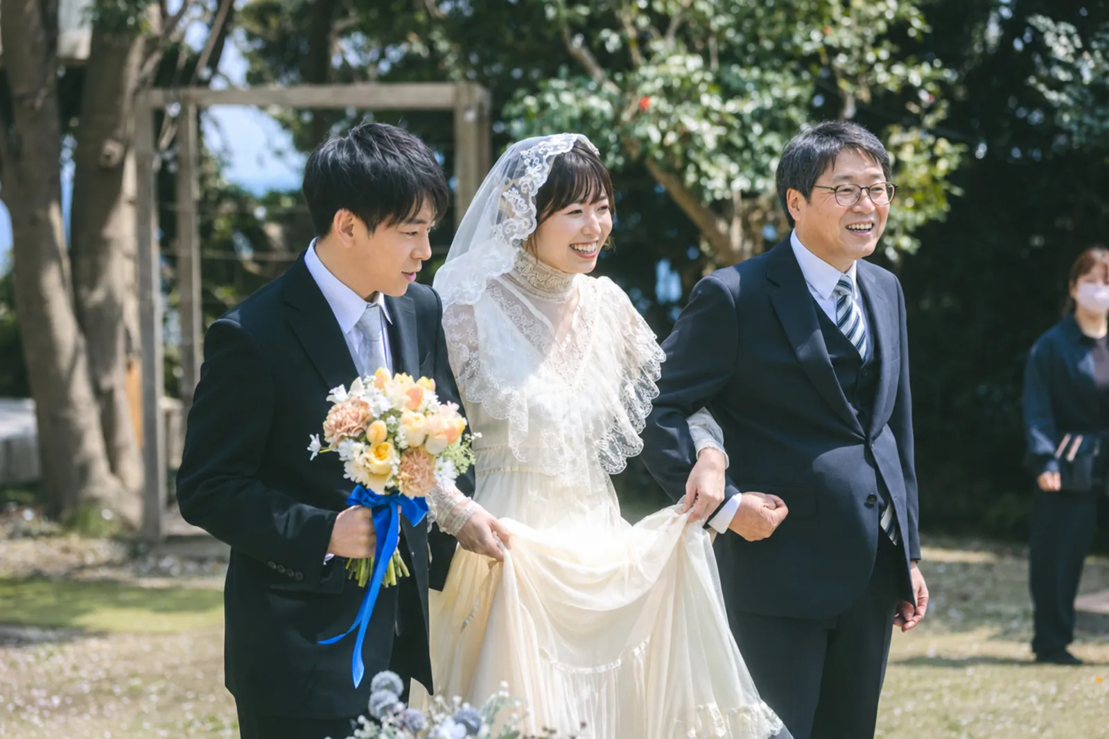 家族に見守られ自然な笑顔でガーデン挙式へ入場する新郎新婦
