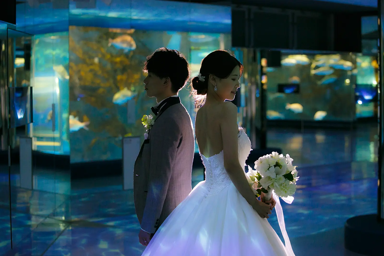 のとじま水族館の館内で背中合わせに立つ洋装姿の新郎新婦