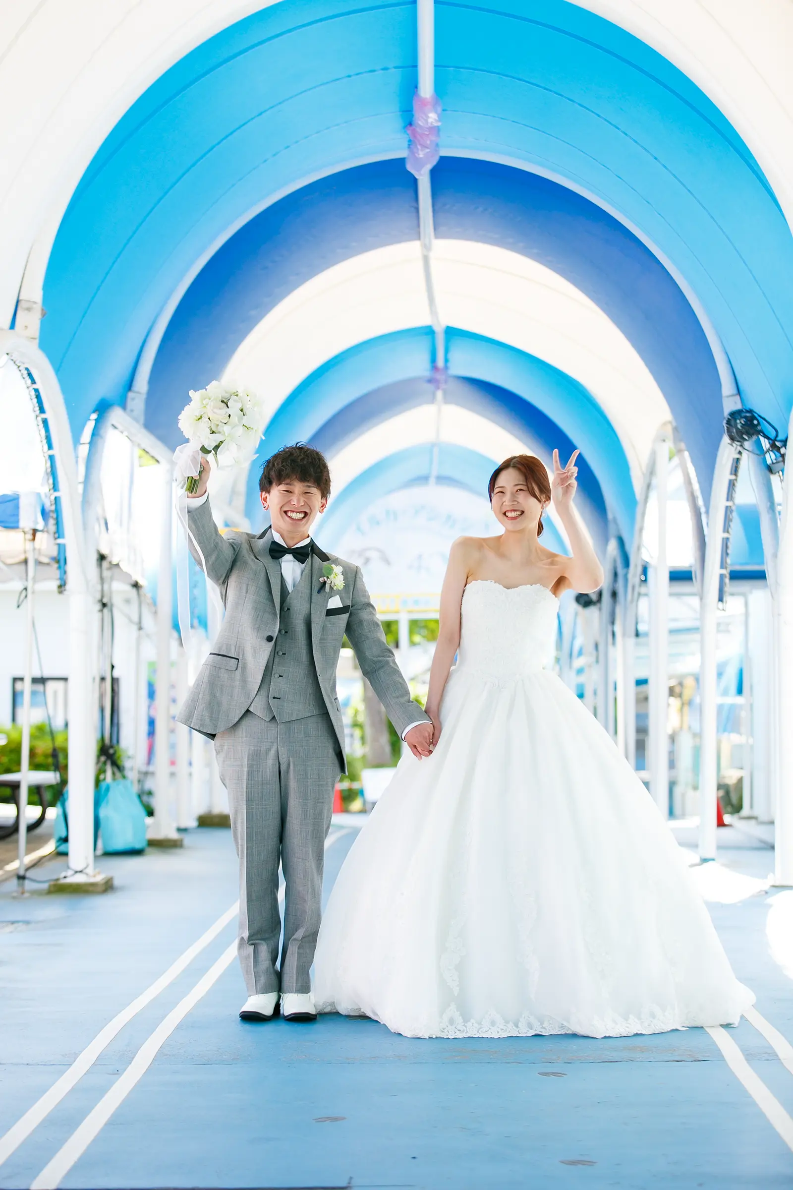のとじま水族館の青い通路で笑顔を見せる洋装姿の新郎新婦