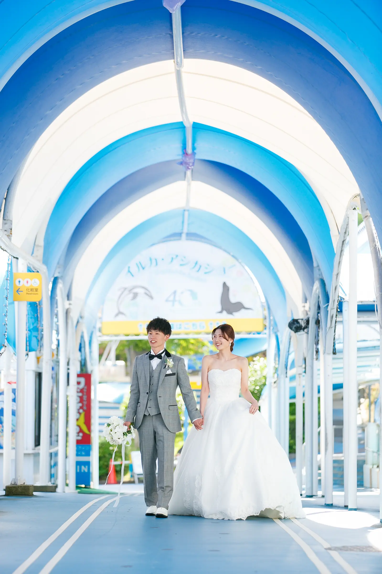 のとじま水族館の青い通路で手をつないで歩く洋装姿の新郎新婦