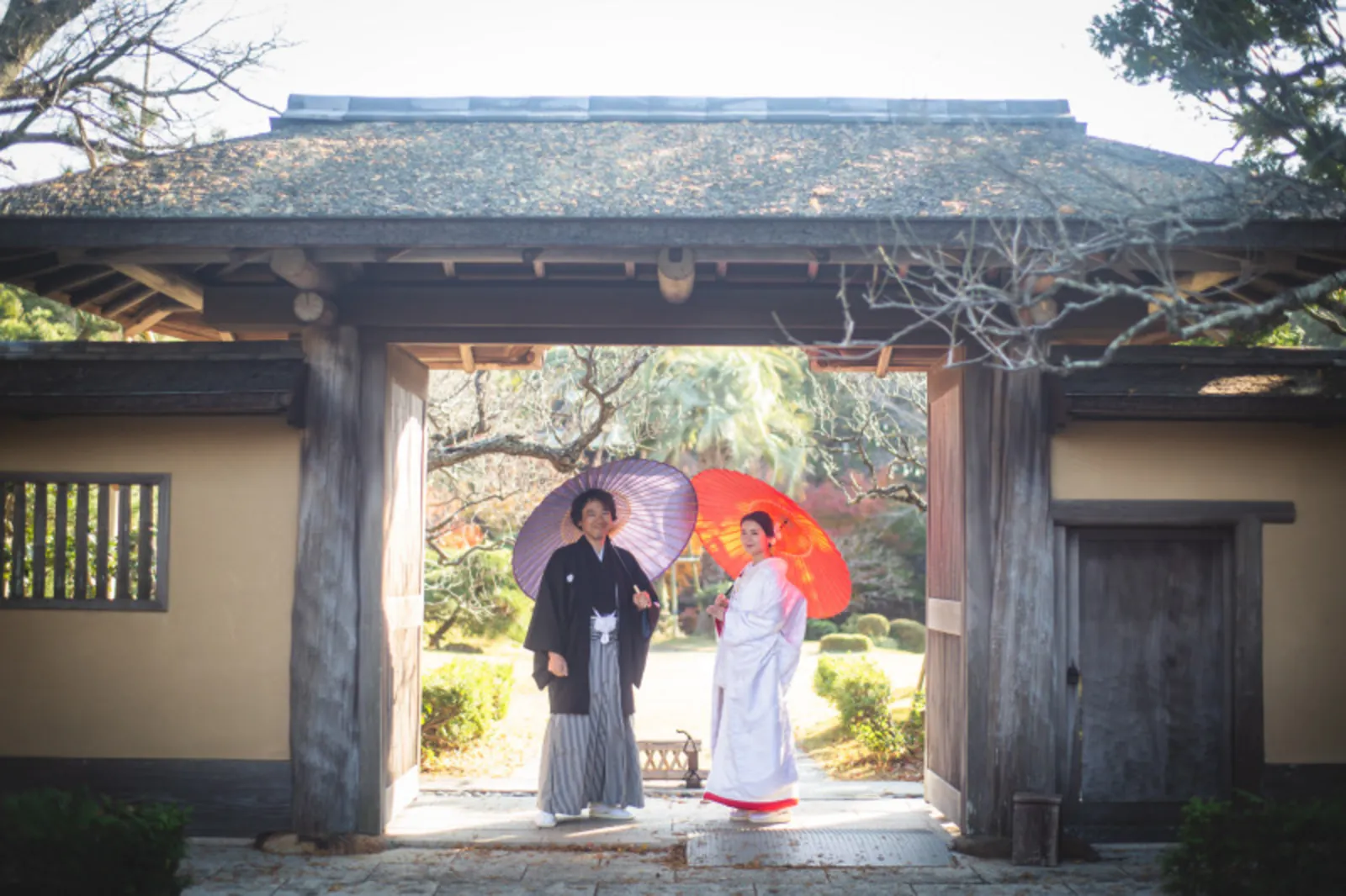 六所神社の門前で和傘を差す和装の新郎新婦の優美なシルエット