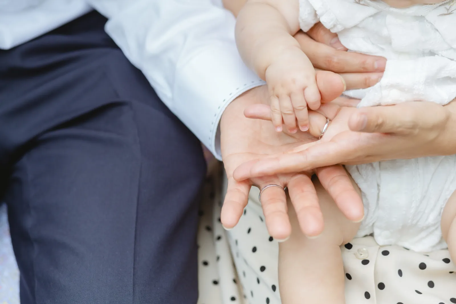 結婚指輪をした両親の手のひらに、赤ちゃんの小さな手が重なるディテール写真
