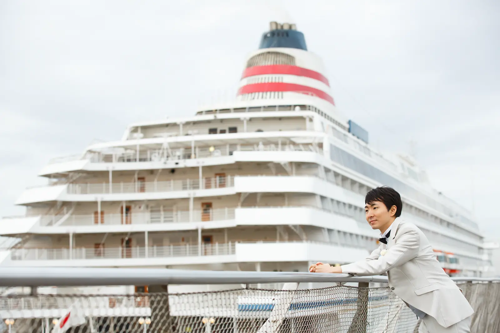 客船を背景に手すりにもたれる新郎のソロポートレート写真