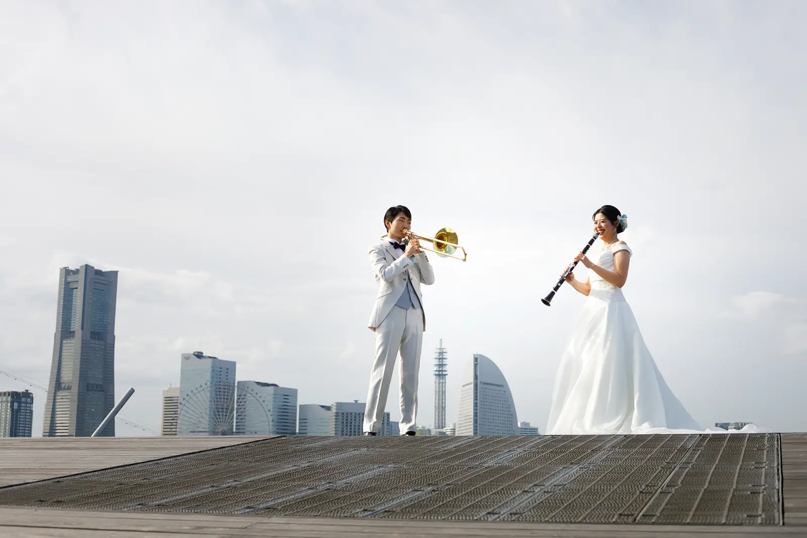 横浜の景色を背景にトロンボーンとクラリネットを演奏する新郎新婦のフォトウェディング写真