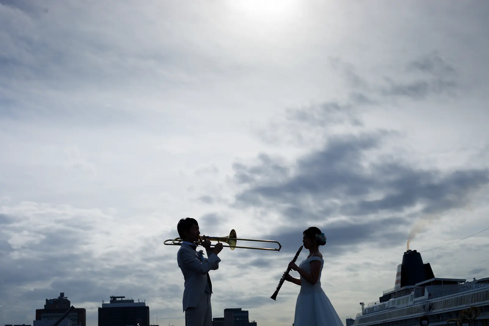 横浜の空を背景にシルエットで向かい合い楽器を演奏する新郎新婦の写真