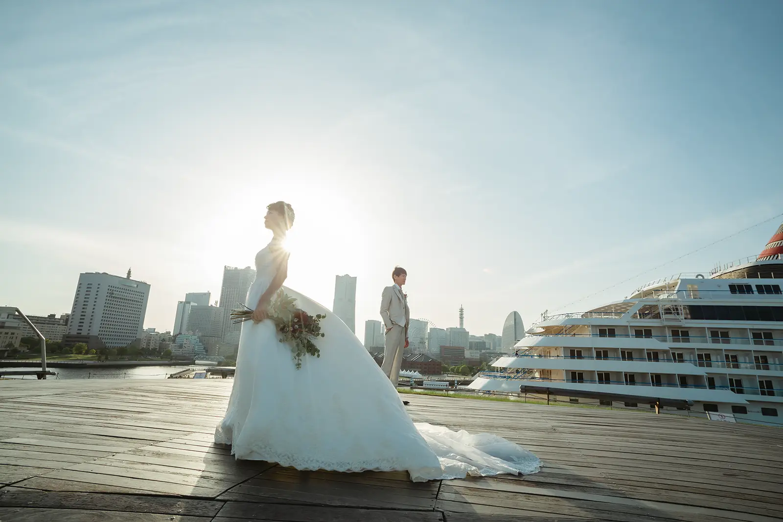 横浜の大さん橋で逆光と客船を背景に立つ新郎新婦