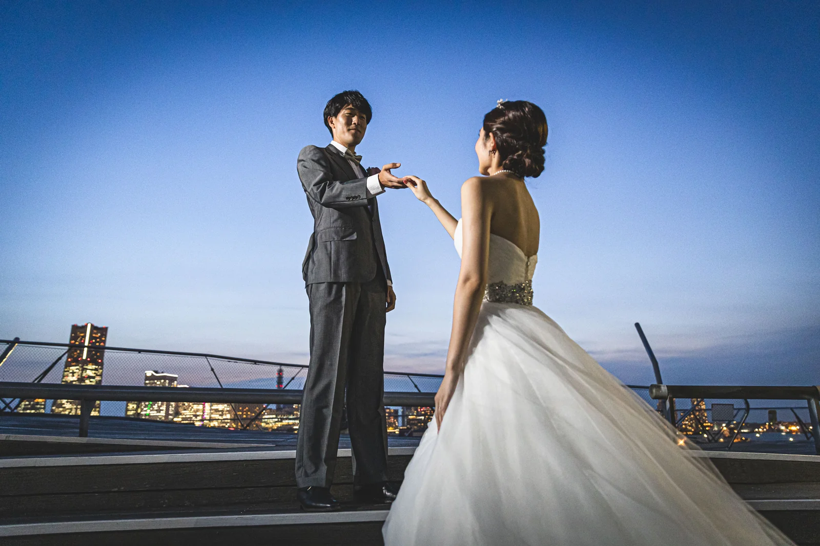 大さん橋のフェンス沿いでみなとみらいの夜景を望む新郎新婦