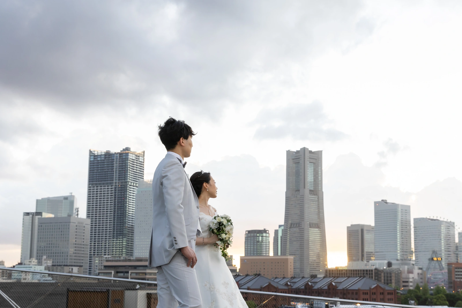 みなとみらいとランドマークタワーを背景に夕暮れの中で撮影する新郎新婦