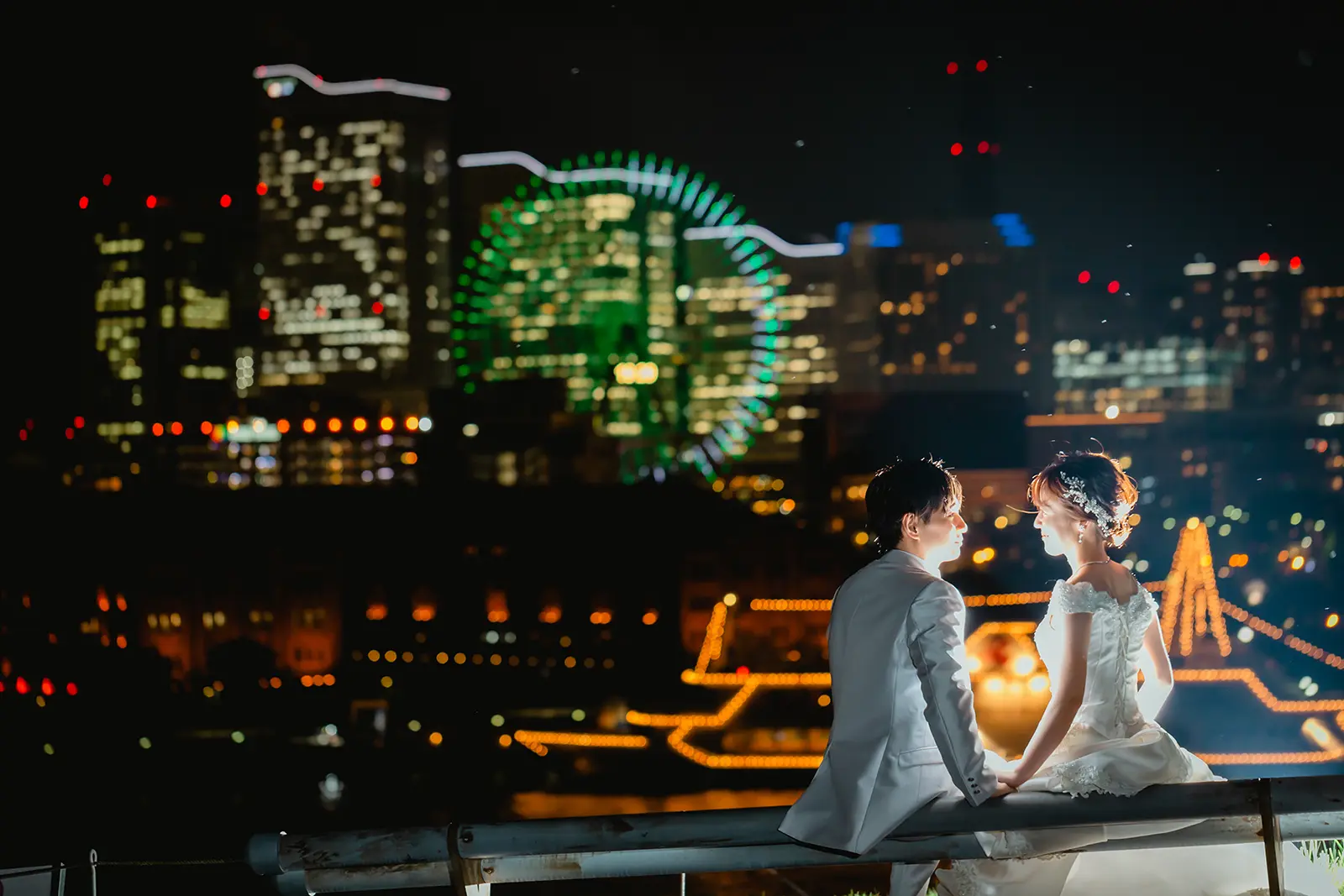 横浜の大さん橋で夜景を背景に座って見つめ合う新郎新婦