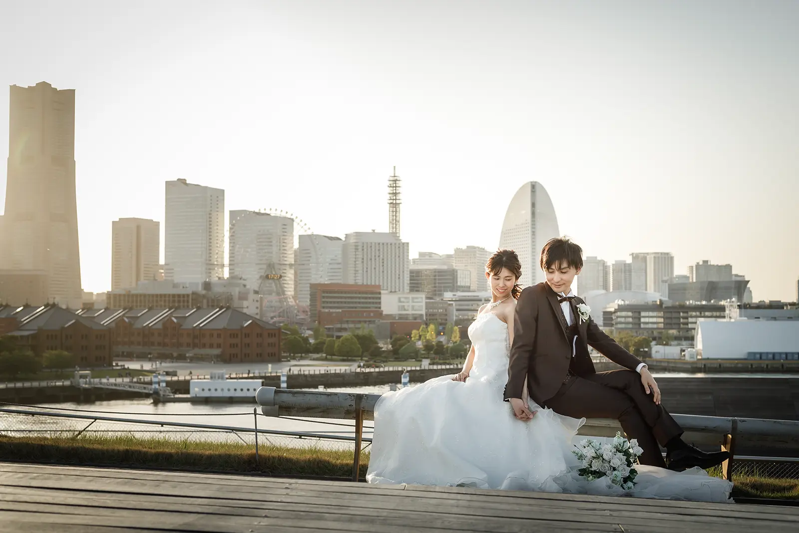 横浜の大さん橋でみなとみらいを背景に座る新郎新婦