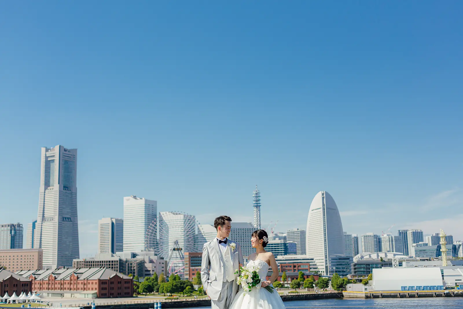 横浜の大さん橋で青空とみなとみらいを背景に立つ新郎新婦