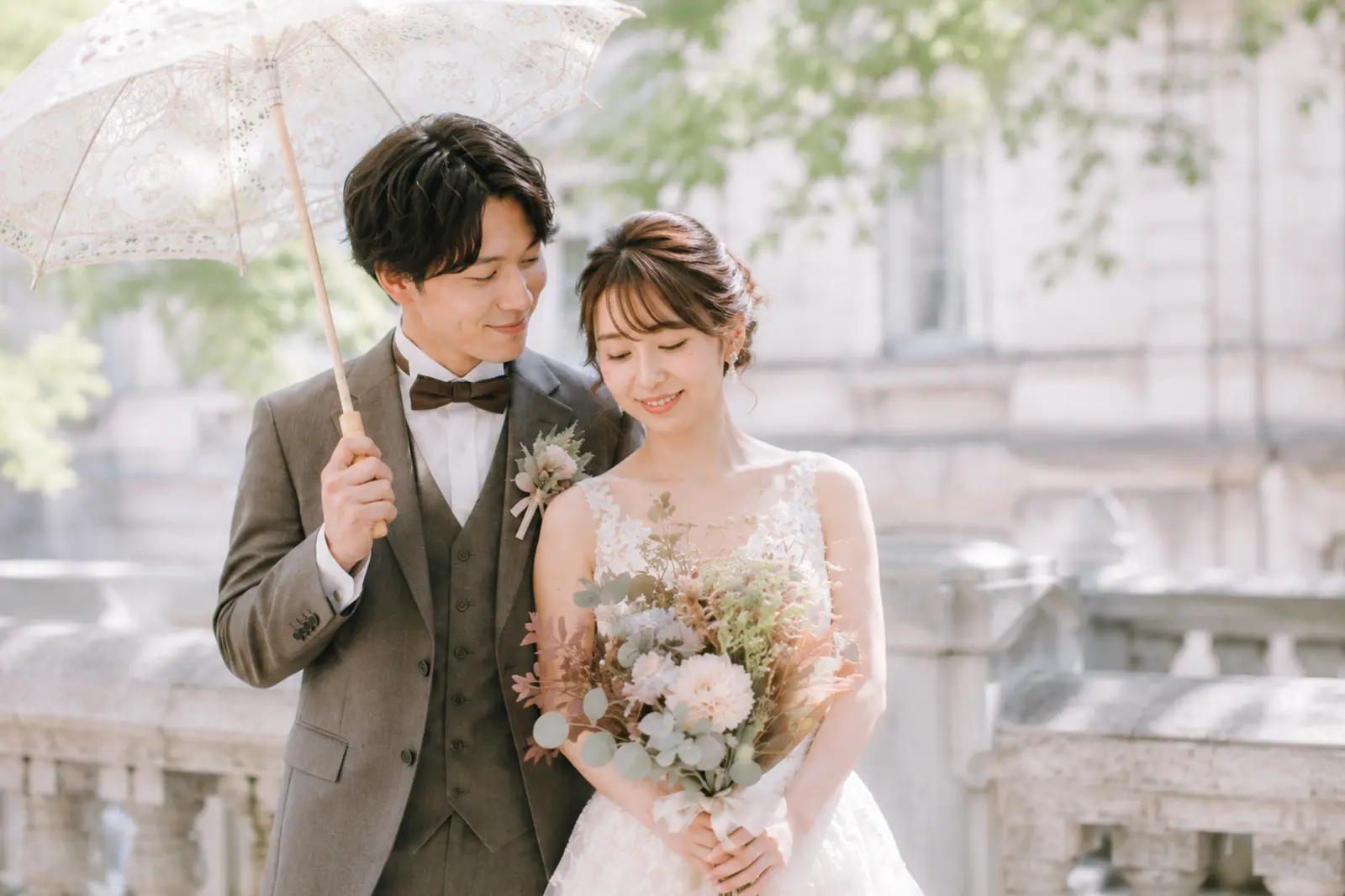新郎新婦が日傘とブーケを使って寄り添う洋装前撮りのポーズ