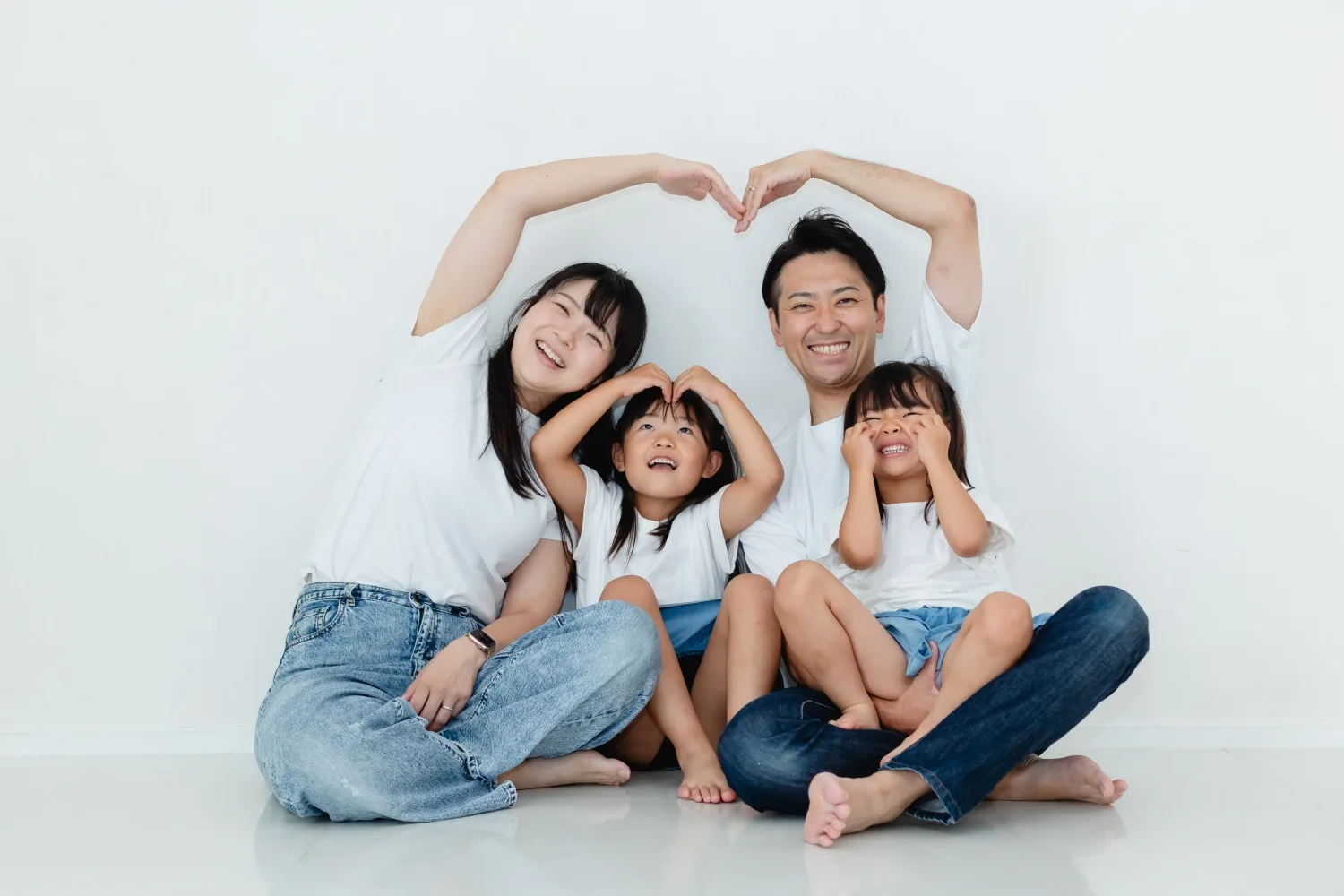 腕でハートを作る家族4人。白いスタジオでの記念撮影