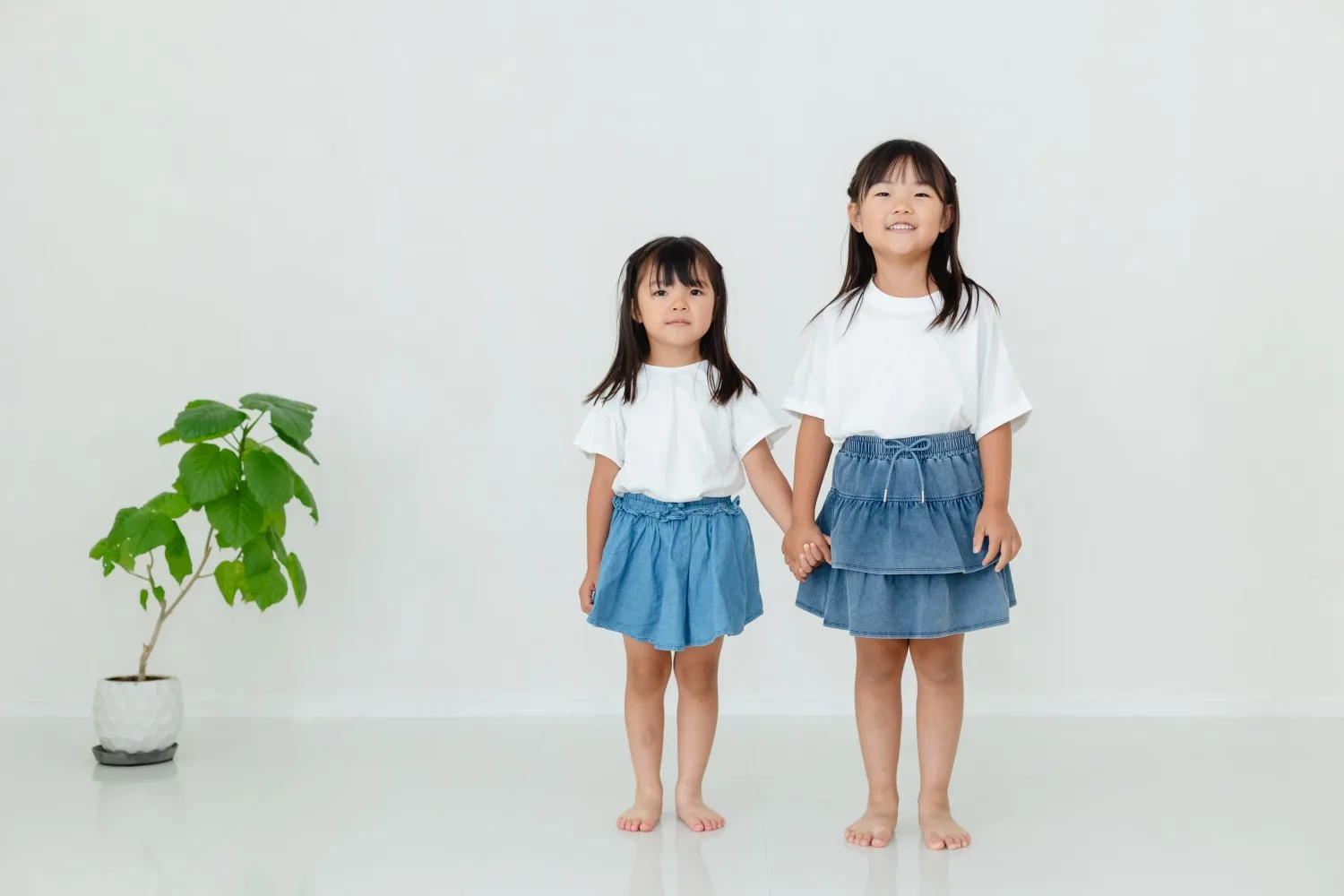 手をつないで立つ姉妹2人の全身写真。白いスタジオでの家族撮影