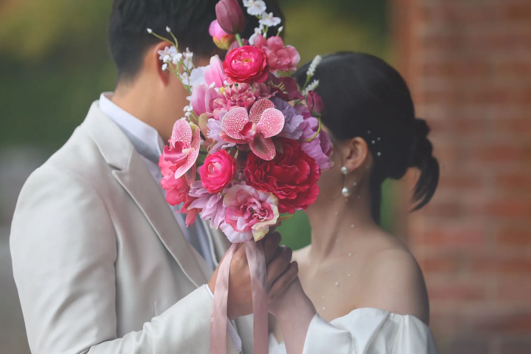 華やかなピンクのブーケで顔を寄せ合うウエディングドレス姿の新郎新婦｜金沢の洋装ロケーションフォトウェディング
