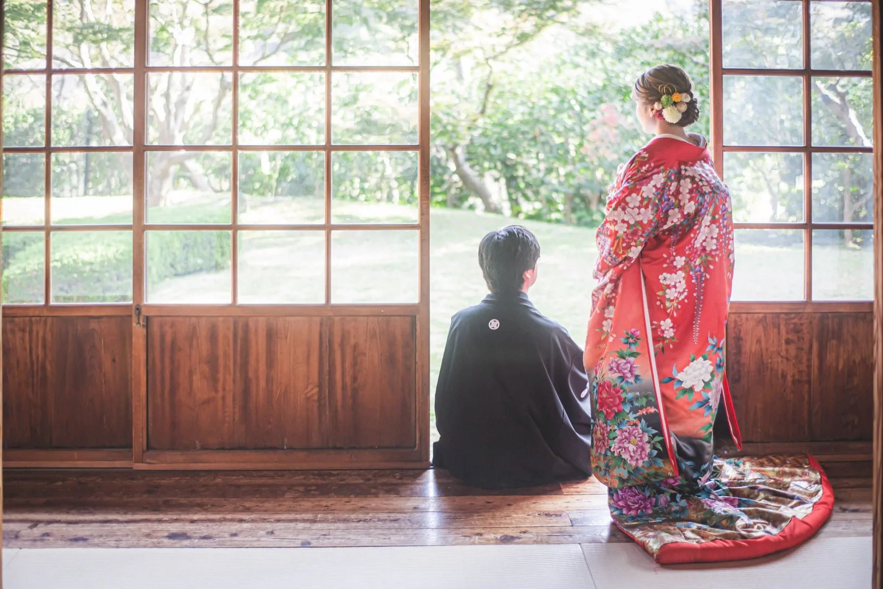 横浜市内の日本庭園の和室で庭を眺める赤い色打掛の花嫁と黒紋付袴の新郎の後ろ姿|横浜の和装ロケーションフォトウェディング