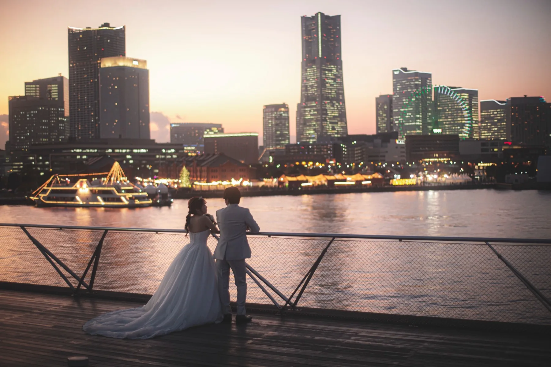 みなとみらいの夜景を望む桟橋でたたずむウエディングドレスの花嫁とスーツの新郎の後ろ姿|横浜の洋装ロケーションフォトウェディング