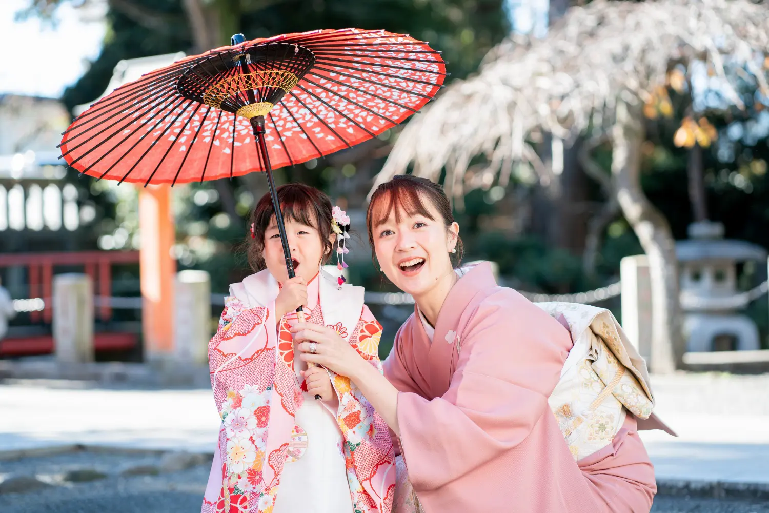 赤い和傘の下で訪問着の母と一緒に笑う被布姿の3歳の女の子、六所神社の七五三（大磯）