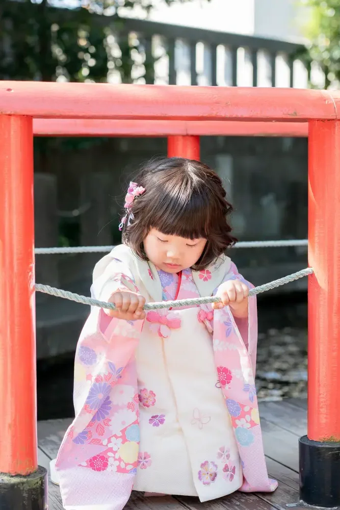 六所神社の橋の上でしゃがみ、白いロープを両手で持つ被布姿の3歳の女の子の七五三撮影