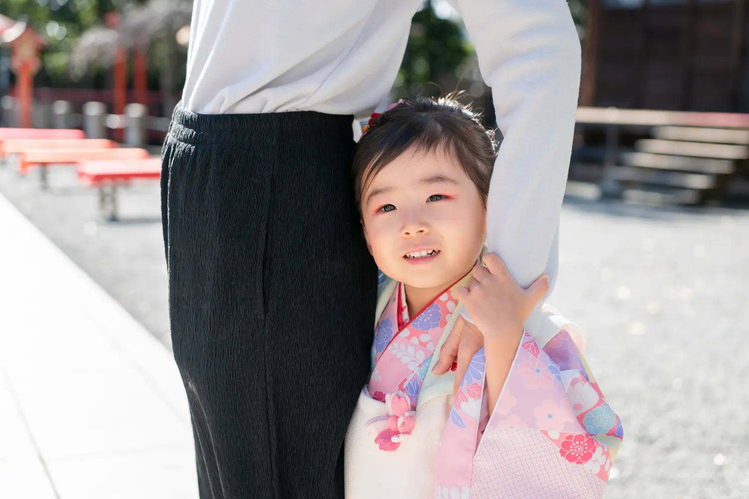 母親の脚に体を預け腕をつかんでカメラを見上げる被布姿の3歳の女の子（七五三・大磯）