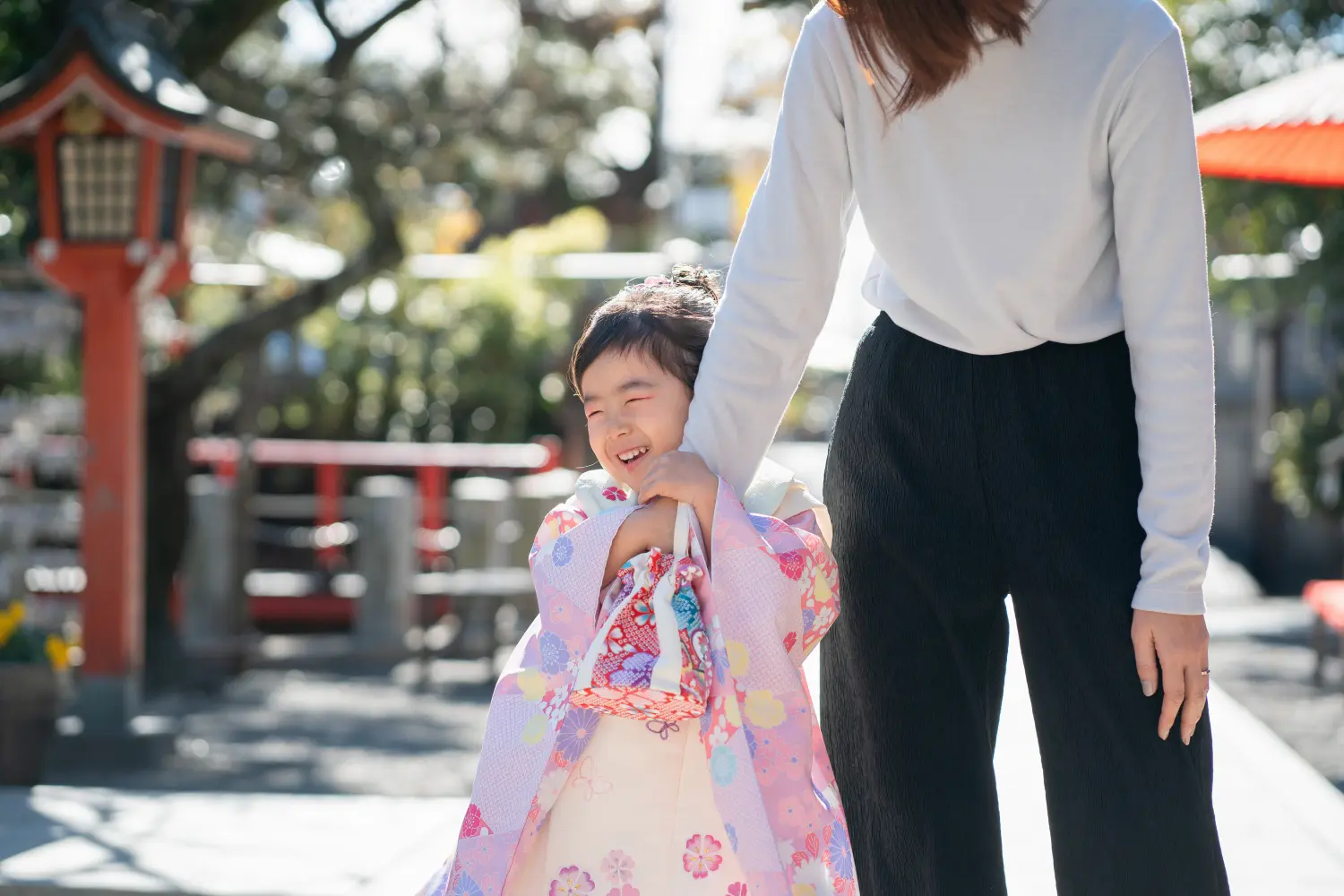 母親の腕にしがみつき目を細めて大笑いする被布姿の3歳の女の子（七五三・六所神社・大磯）